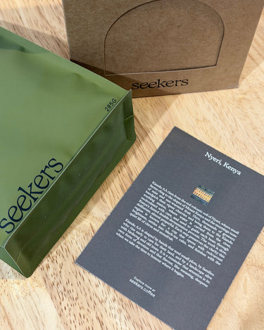 Green bag with 'seekers' branding on a wooden surface with a brown box and black paper.